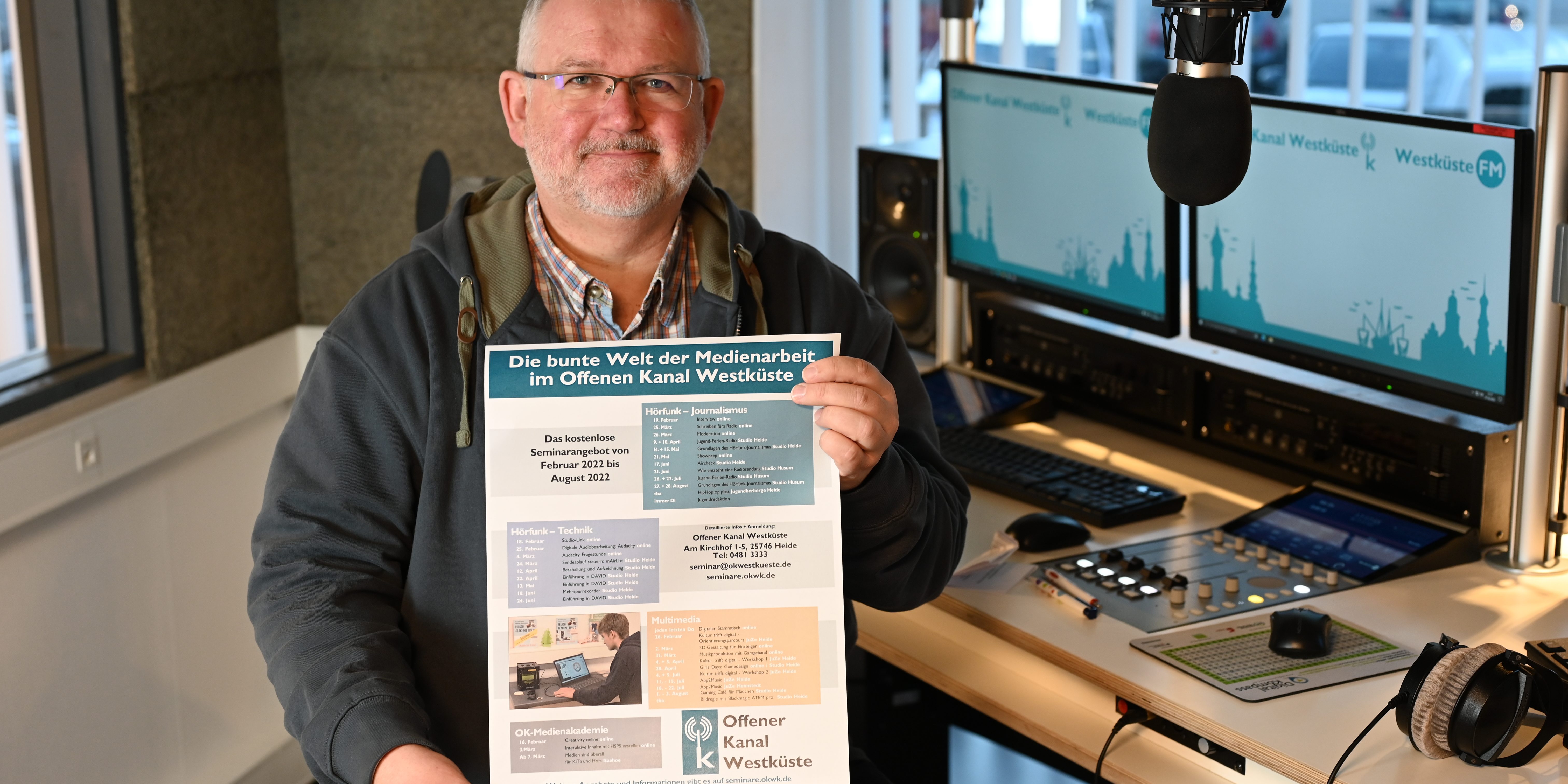 Andreas Guballa hält das eigene Plakat mit den OK Westküste Seminaren in die Kamera